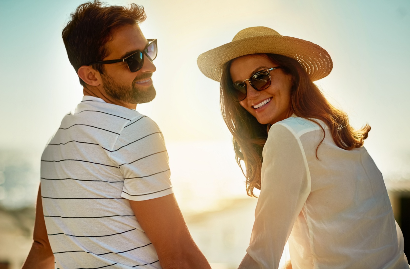 A smiling couple wearing sunglasses outdoors, while enjoying the sunny weather.